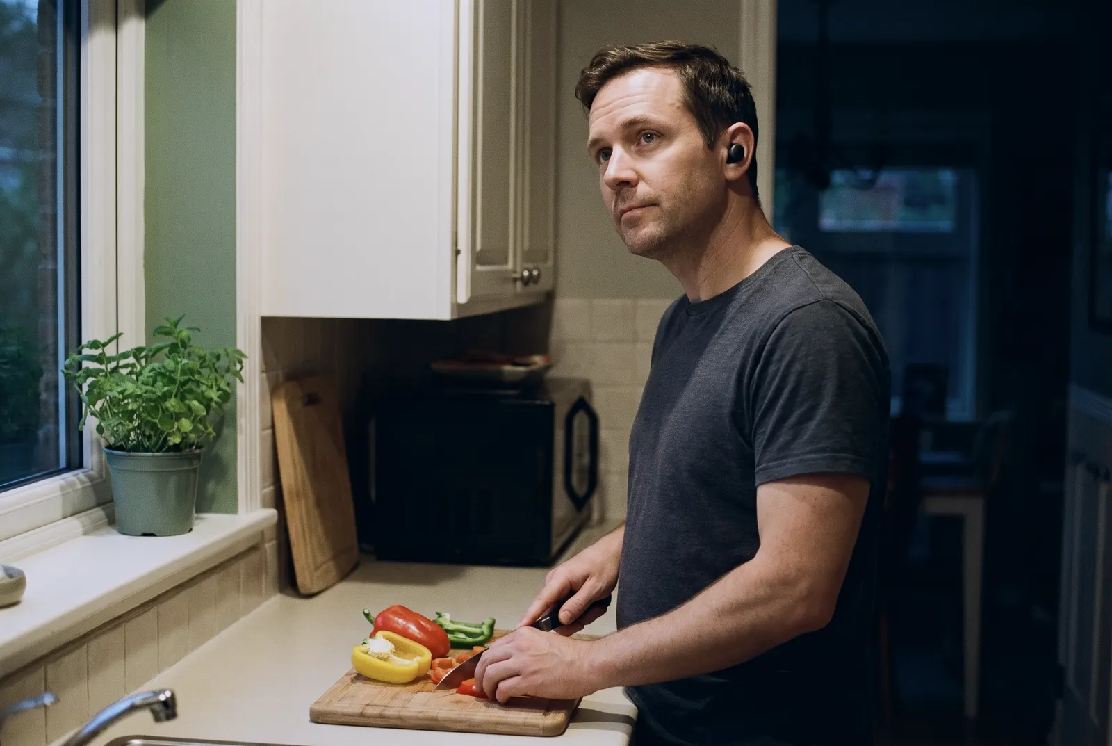 A man with earbuds slices peppers in his kitchen